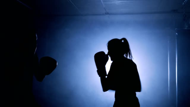 Silhouettes-of-a-female-boxer-punching-a-boxing-bag-with-boxing-gloves-in-a-smoky-gym