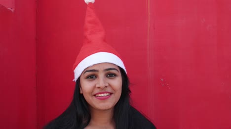 Close-up-portrait-of-young-Indian-girl-with-Santa's-hat-making-faces-towards-the-camera,-excited-and-extremely-happy