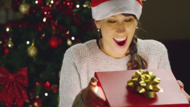 Girl-with-Christmas-hat-makes-wishes-and-opens-a-Christmas-gift-package.-concept-of-holidays-and-new-year.-the-girl-is-happy-and-smiles-with-christmas-gift-in-hand.
