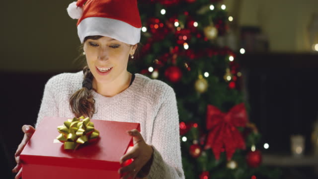 Girl-with-Christmas-hat-makes-wishes-and-opens-a-Christmas-gift-package.-concept-of-holidays-and-new-year.-the-girl-is-happy-and-smiles-with-christmas-gift-in-hand.
