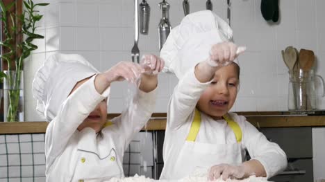 Zwei-kleine-Mädchen-in-der-Küche-zubereiten,-ein-Dessert-für-die-Familie.-Wie-sie-lernen,-zu-kochen-beginnen-sie-das-Spiel-mit-Mehl-und-lächelnd-einander.