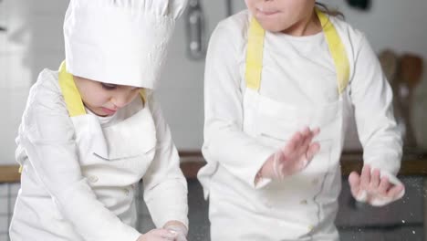 Dos-niñas-en-la-cocina-preparan-comida,-un-postre-para-la-familia.-Como-aprender-a-cocinar-empiezan-jugando-con-harina-y-sonriendo-unos-a-otros.