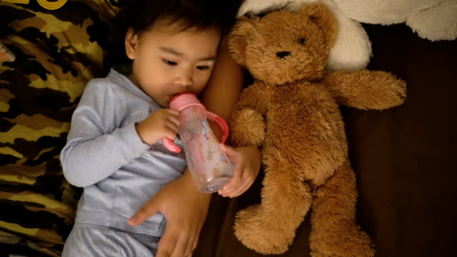 Asiatische-Mädchen-essen-Milch-mit-einer-Flasche,-halten-Teddybär