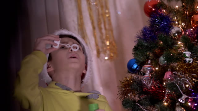 boy-in-a-Santa-Claus-hat-blowing-soap-bubbles-on-the-background-of-a-New-Year-tree