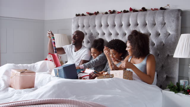 Junge-Mischlinge-Familie-sitzt-oben-im-Bett-zusammen-Auspacken-Geschenke-am-Weihnachtsmorgen