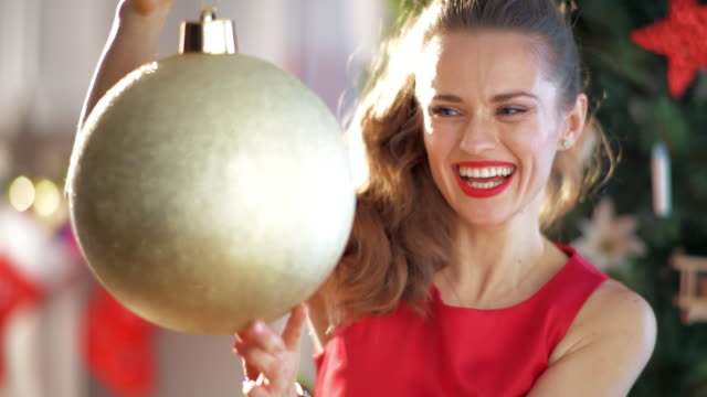 housewife-near-Christmas-tree-spinning-big-gold-Christmas-ball
