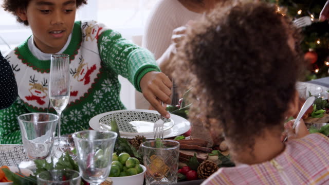 Multi-generation-mixed-race-family-sitting-at-Christmas-dinner-table-eating-together,-panning-shot