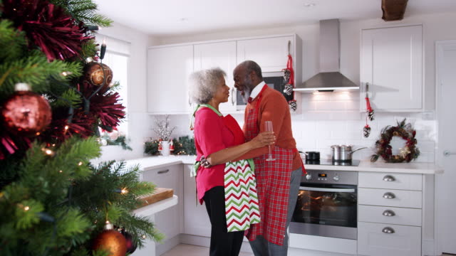 Feliz-pareja-madura-negro-sosteniendo-copas-de-champagne,-riendo-y-bailando-en-la-cocina-preparando-la-cena-de-Navidad,-vista-lateral