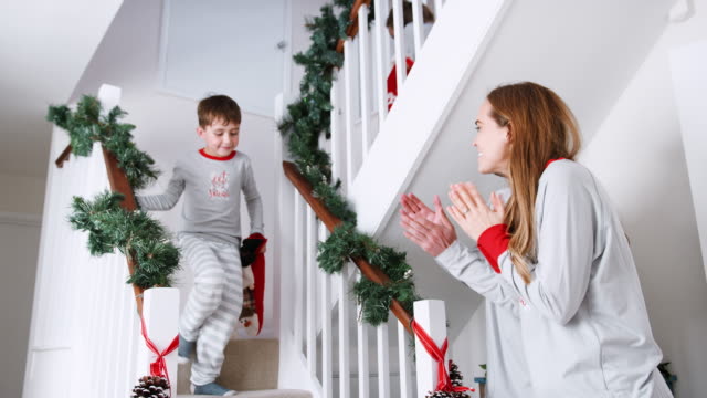 Los-padres-saludo-emocionado-a-niños-vistiendo-pijamas-bajando-escaleras-con-medias-en-la-mañana-de-Navidad