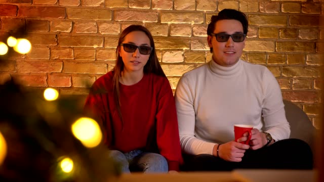 Kaukasische-paar-in-3D-Brille-auf-Sofa-sitzen-und-Film-mit-Tasse-Getränk-wird-in-weihnachtliche-Stimmung-schockiert.