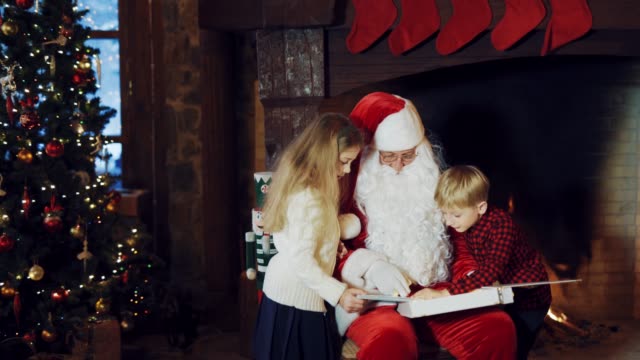 Santa-Claus-zeigt-ein-Album-mit-Fotos-für-Kinder-auf-dem-Hintergrund-eines-Kamins-mit-Weihnachten-Socken-und-mit-einem-Weihnachtsbaum-im-Zimmer,-aber-der-junge-in-einem-karierten-Hemd-flieht.