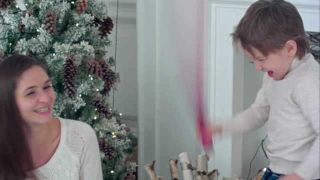 Happy-mother-and-son-having-wrapping-paper-sword-fight-near-the-Christmas-tree