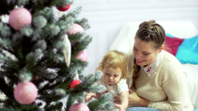 Happy-young-mother-playing-with-her-sweet-baby-in-a-decorated-room-near-the-christmas-tree