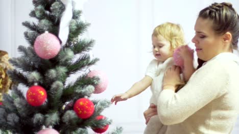 Glückliche-junge-Mutter-mit-ihrem-süßen-Baby-in-einem-eingerichteten-Raum-in-der-Nähe-der-Weihnachtsbaum-spielen