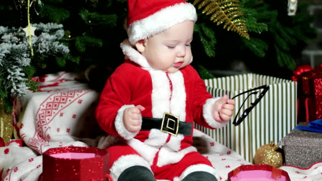 Santa-Claus-niño,-niño-en-traje-de-Santa,-jugar-con-gafas,-niño-se-sienta-en-el-carnaval-de-disfraces,-trajes-de-la-Navidad-bajo-el-árbol-de-Navidad