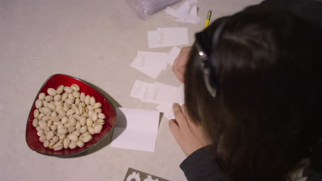 Una-chica-sentada-en-un-mostrador-de-cocina-dibujando-en-trozos-de-papel,-con-snacks