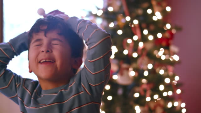 Junge-tanzt-mit-winzigen-Santa-Hut-auf-und-dann-stellt-sie-auf-eine-Miniatur-Weihnachtsbaum