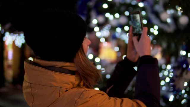 Young-woman-in-bright-winter-clothes-taking-photo-with-mobile-phone-at-the-Christmas-market