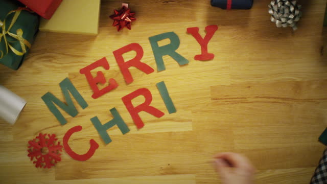 Top-View-Time-Lapse-of-a-Hand-Laying--Words-"Merry-Christmas"-Made-of-Colourful-Paper-Letters.