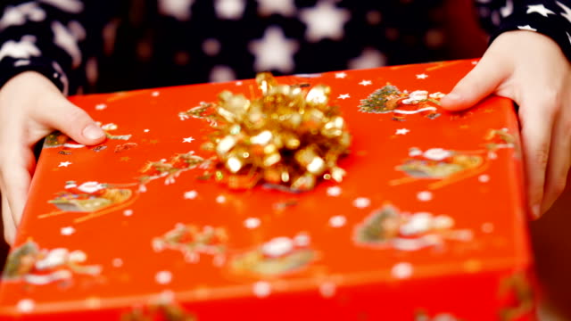 Cerca-de-dos-manos-del-niño-con-un-regalo-de-Navidad-en-una-envoltura-de-papel-de-color-hermoso-con-un-arco-de-oro