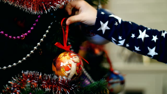 Close-up-of-child-girl-hands-are-decorating-a-Christmas-tree-with-bright-colorful-Christmas-toys,-balls