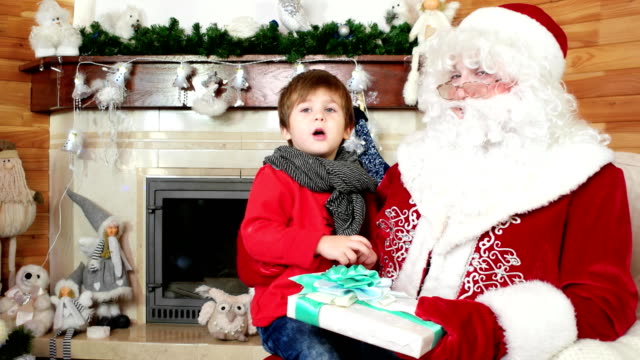 kleiner-Junge-erzählt-Santa-seine-Weihnachtswünsche,-Kind-sitzt-auf-Saint-Nicolas-Schoß,-großes-Geschenk-für-Kind