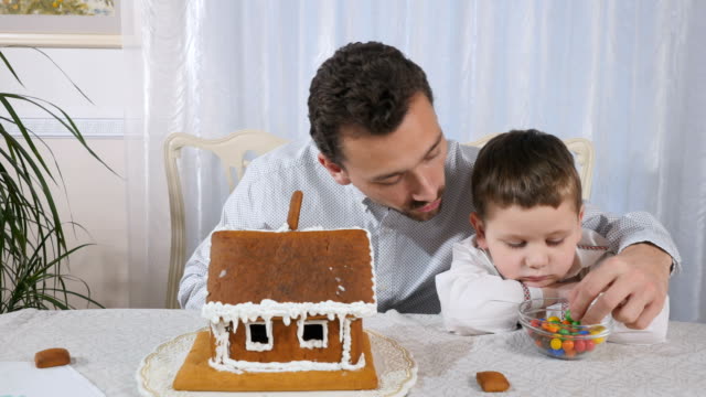 The-father-tells-how-decorate-a-gingerbread-house-to-a-little-son