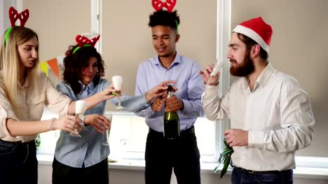 Atractivo-joven-oficinistas-abriendo-una-botella-de-vino-espumoso,-celebrando-Navidad-y-año-nuevo-en-la-oficina.-Compañeros-felizes-celebrando-en-la-oficina