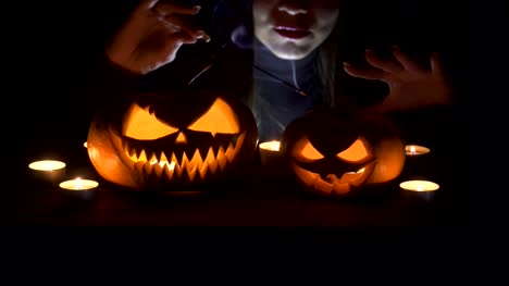 On-the-main-terms-of-the-pumpkin,-witch-casts-a-spell-from-behind..-Beautiful-young-woman-in-witches-hat-and-costume-holding-carved-pumpkin.-Halloween-art-design