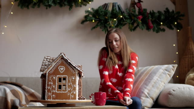 Beautiful-woman-wearing-winter-outfit-drinking-tea-with-gingerbread-at-home-near-Christmas-tree