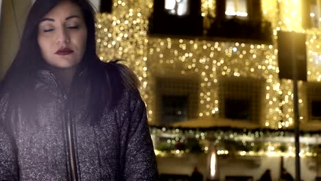 sad-woman-looks-at-the-camera,-while-behind-light-up-the-Christmas-lights