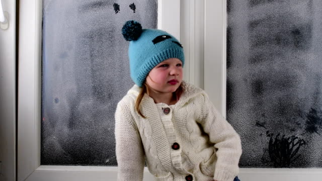 Small-girl-sits-on-windowsill-behind-the-frozen-window.