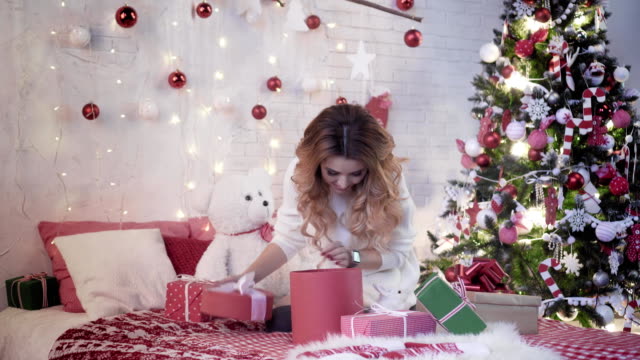 Junge-attraktive-Frau-sitzt-auf-einem-Bett-in-der-Nähe-der-Weihnachtsbaum-und-packt-Geschenke