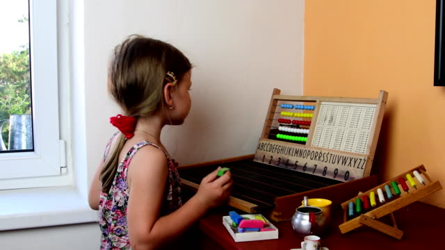 Sweet-little-girl-plays-with-abacus-and-writes-on-blackboard-with-chalk.-Preschool-concept,-childhood-concept.-Toy-abacus-with-Czech-alphabet.-Cute-girl-like-preschooler