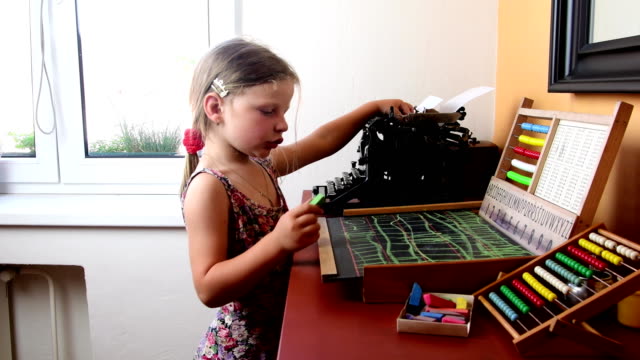 Sweet-little-girl-plays-with-abacus-and-writes-on-blackboard-with-chalk.-Preschool-concept,-childhood-concept.-Toy-abacus-with-Czech-alphabet-and-vintage-typewriter.-Cute-girl-like-preschooler