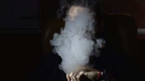 junge-bärtiger-Mann-in-Gläsern-raucht-eine-Wasserpfeife-und-Ausblasen-Rauch-Closeup-auf-schwarzem-Hintergrund-in-Zeitlupe-in-4k