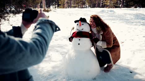 Couple-having-fun-taking-photos-with-snowman-in-the-snow