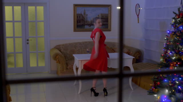 Beautiful-sexy-woman-in-red-dress-dance-in-the-room-celebrating-Christmas-alone