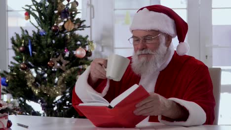 Santa-Claus-ist-aus-einer-Tasse-trinken-und-ein-Buch-zu-lesen