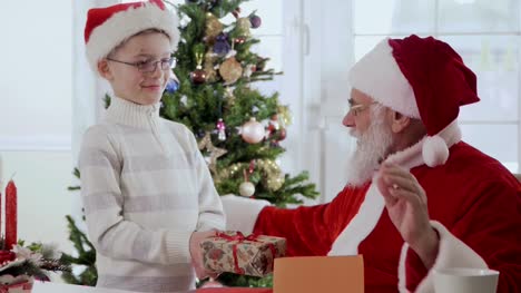 Niño-da-Santa-Claus-un-regalo-mientras-que-él-está-leyendo-la-carta-del-deseo