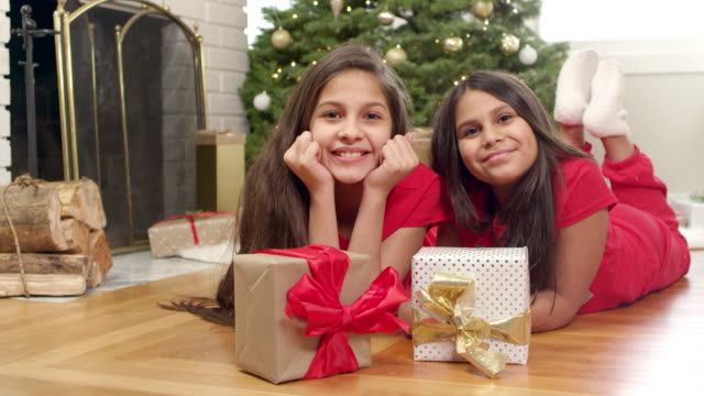 Zwei-Mädchen-liegen-auf-dem-Boden-vor-einem-Baum-und-Ihre-Weihnachten-präsentiert-sitzen-am-Boden-neben