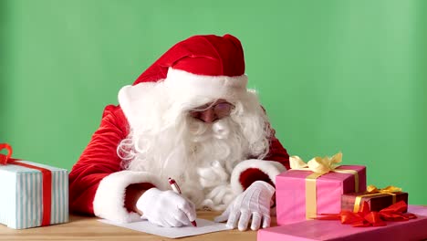 Divertido-Santa-Claus-escribe-una-carta,-mira-a-la-cámara-y-agita-su-mano,-un-saludo-firme,-chromakey-en-el-fondo