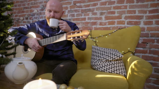 Man-drinking-tea-and-playing-guitar-next-to-Christmas-tree