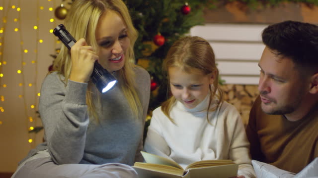 Padres-felices-leyendo-cuento-de-hadas-con-hija-en-víspera-de-Navidad