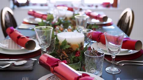 Tilt-shot-of-a-Christmas-dinner-table-with-seasonal-decorations,-crystal-glasses-and-Christmas-crackers-on-plates,-elevated-view