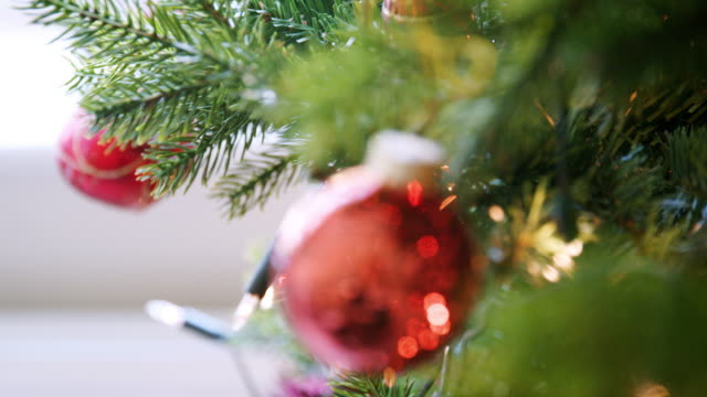 Handheld,-shallow-depth-of-field-close-up-of-glittering-baubles-hanging-on-a-Christmas-tree-with-fairy-lights