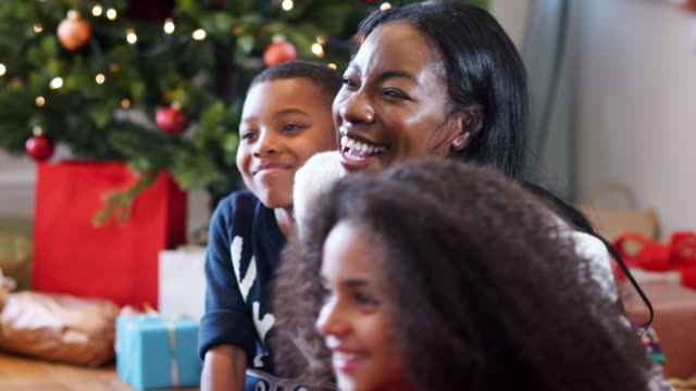 Aufgeregten-Kinder-sitzen-am-Boden-mit-Mutter-als-Familie-gemeinsam-Weihnachten-feiern
