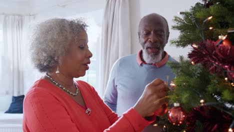 Senior-pareja-colgando-adornos-de-árbol-de-Navidad-en-casa-junto