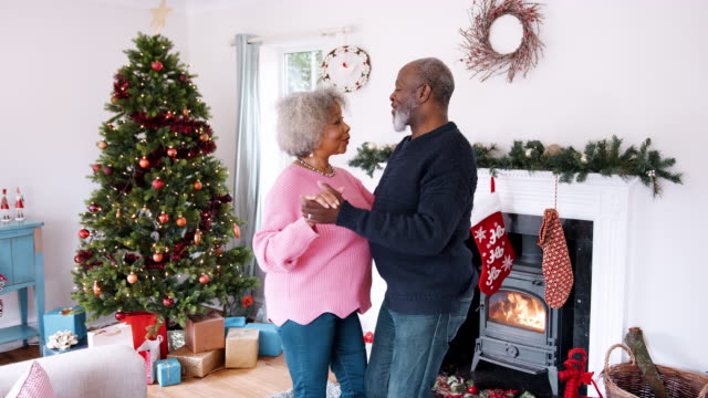 Ältere-schwarze-Paare-tanzen-in-ihrem-Wohnzimmer-dekoriert-für-Weihnachten,-Dreiviertel-Länge-Ansicht,-handheld