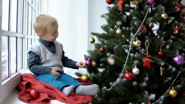 Little-baby-boy-decorating-a-Christmas-tree-toys.-Holidays,-gift,-and-new-year-concept